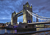 Die Tower Bridge ist in der Abenddämmerung beleuchtet und spiegelt sich im ruhigen Wasser der Themse; London, England