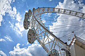 View from directly below the cables and pods of the London Eye with a blue sky and clouds in the background; London, England