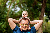 Ein Vater hält sein kleines Mädchen auf den Schultern und sie hält seinen Kopf, während er im Herbst draußen ist; Edmonton, Alberta, Kanada