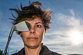 Frau mit zerzauster Frisur hält einen Golfschläger an ihr Auge; Schweiz
