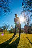 Golferin mit Putter am Loch eines Golfplatzes, von der Sonne angestrahlt; Schweiz
