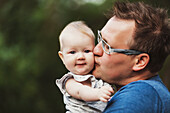 Ein Vater hält sein kleines Mädchen im Arm und kuschelt und küsst es im Herbst im Freien; Edmonton, Alberta, Kanada