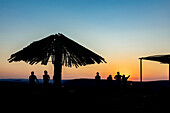 Silhouettierte Touristen und Regenschirm bei Sonnenuntergang, Blick über den Fish River Canyon; Namibia