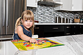 Ein süßes kleines Mädchen, das in der Küche ein Buch liest und in die Kamera schaut: Edmonton, Alberta, Kanada