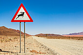 Achtung-Wildtier-Schild an einer langen Trockenstraße, Namib-Wüste, Namib-Naukluft-Nationalpark; Namibia