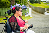 Maori-Frau mit Cerebralparese in einem Rollstuhl, die einen Bürgersteig hinunterfährt; Wellington, Neuseeland