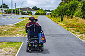 Maori woman with Cerebral Palsy in a wheelchair going down a sidewalk; Wellington, New Zealand