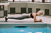 Frau trainiert auf einer Matte und macht eine Planke neben einem Pool; Wellington, Neuseeland