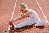 Woman sits to stretch her leg muscles to prepare for running on a track; Wellington, New Zealand