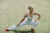 Woman stretching her leg muscles on a grass field; Wellington, New Zealand