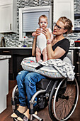 A paraplegic mother holding her baby on her lap, in her kitchen, while sitting in her wheel chair: Edmonton, Alberta, Canada