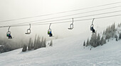 Downhill skiers ride on a chairlift through the clouds, Sun Peaks Resort; Sun Peaks, British Columbia, Canada