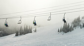 Abfahrtsläufer fahren mit einem Sessellift durch die Wolken, Sun Peaks Resort; Sun Peaks, British Columbia, Kanada