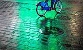 Cyclist riding bike on wet walkway with glowing green light at night in Manhattan; New York City, New York, United States of America