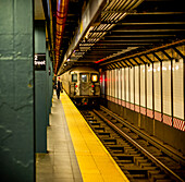 Underground subway on tracks with people walking on platform; New York City, New York, United States of America