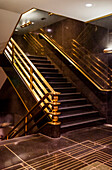 Staircase with brass handrails inside a building with dark brown flooring and walls; New York City, New York, United States of America