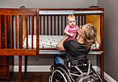A paraplegic mother picking her baby up after a sleep in a customized crib with a sliding door; Edmonton, Alberta, Canada