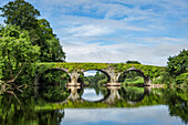 Alte Steinbrücke über den Blackwater-Fluss in Kilavullen, die sich an einem sonnigen Sommertag im Wasser spiegelt; Killavullen, Grafschaft Cork, Irland