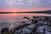 Sun setting over lake with reflections on a cloudy evening with limestone rocks with cracks on the shore in the foreground, Burren National Park; County Clare, Ireland