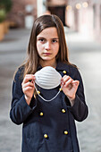 Young girl stands holding a protective mask to protect against COVID-19 during the Coronavirus World Pandemic; Toronto, Ontario, Canada