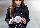 Young girl stands holding protective mask in her hands during the Coronavirus World Pandemic; Toronto, Ontario, Canada