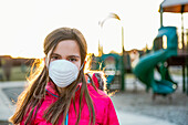 Young girl stands at a playground wearing a protective mask to protect against COVID-19 during the Coronavirus World Pandemic; Toronto, Ontario, Canada