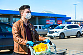 A young man stands in a parking lot with a grocery cart during the Covid-19 World Pandemic; Edmonton, Alberta, Canada