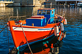 Small traditional orange, white and blue Greek fishing boat with boat fenders docked in Mykonos new port marina at sunrise; Mykonos Town, Mykonos Island, Greece