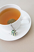 Tasse Tee mit Tee-Ei und losen Teeblättern auf Untertasse