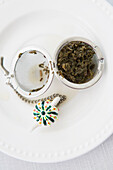 Overhead View of Used Tea Infuser Open with Loose Tea Leaves on Saucer, Studio Shot