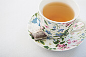 Cup of tea in pretty floral cup with saucer and used tea bag, on white background, studio shot