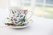 Cup of tea in pretty floral cup with saucer and used tea bag, studio shot