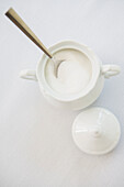 Zuckerdose aus weißem Porzellan mit Zucker und Löffel, Atelieraufnahme