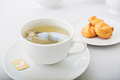 Tasse Tee in weißer Porzellantasse mit Untertasse und Teller mit Kokosmakronen, Studioaufnahme