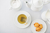 Teetasse aus weißem Porzellan mit Untertasse, Zuckerdose, Milchkännchen, Teekanne und Teller mit Kokosmakronen, Atelieraufnahme