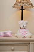 Ein Stapel Babydecken auf der Kommode neben einem Teddybär und einer Lampe im Kinderzimmer
