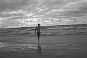 Rückenansicht eines Jungen, der in der Brandung am Strand läuft