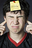 Boy Plugging Ears with Note Pinned to Forehead