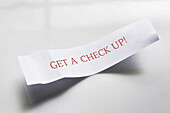 Close-up of message from fortune cookie on white plate, showing text for medical checkup, studio shot on white background