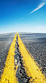 Close-up view of yellow center lines on deserted highway with blue sky, Canada