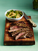 Sliced Flank Steak and Salad on Wooden Cutting Board with Knife on Turquoise Background in Studio