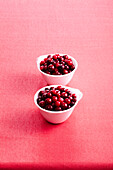 Cranberries in bowls on red background, studio shot
