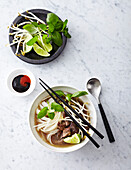 Beef Pho Noodle Soup in bowl with condiments, studio shot