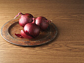 Rote Zwiebeln auf einem Metallteller vor einem hölzernen Hintergrund, Studioaufnahme