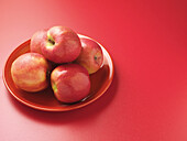 Rote Äpfel auf Teller, roter Hintergrund, Studioaufnahme