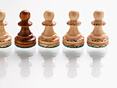 Dark wooden chess piece in row of light wooden chess pieces