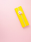 Gift wrapped in yellow wrapping paper on pink background, studio shot