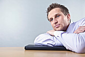 Businessman Leaning on Desk Looking Thoughtful
