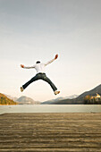 Mann auf dem Steg springt hoch in die Luft, Fuschlsee, Salzburger Land, Österreich