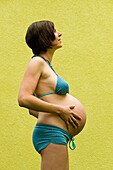 Profil einer im neunten Monat schwangeren Frau, die ihren Bauch berührt